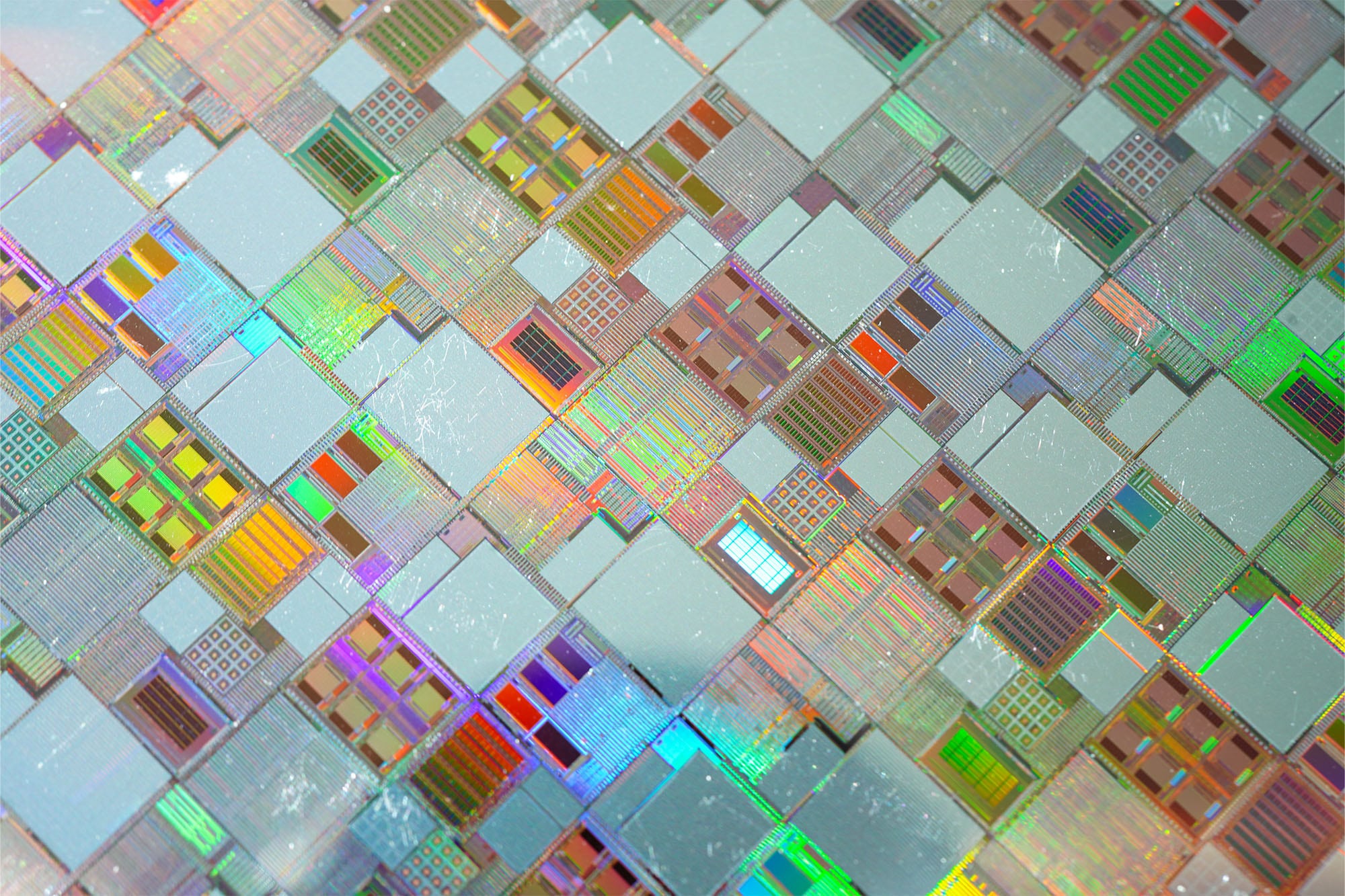 Close-up of colorful silicon microchips arranged in a diagonal grid, showing square dies and interconnect patterns for an abstract circuit design.