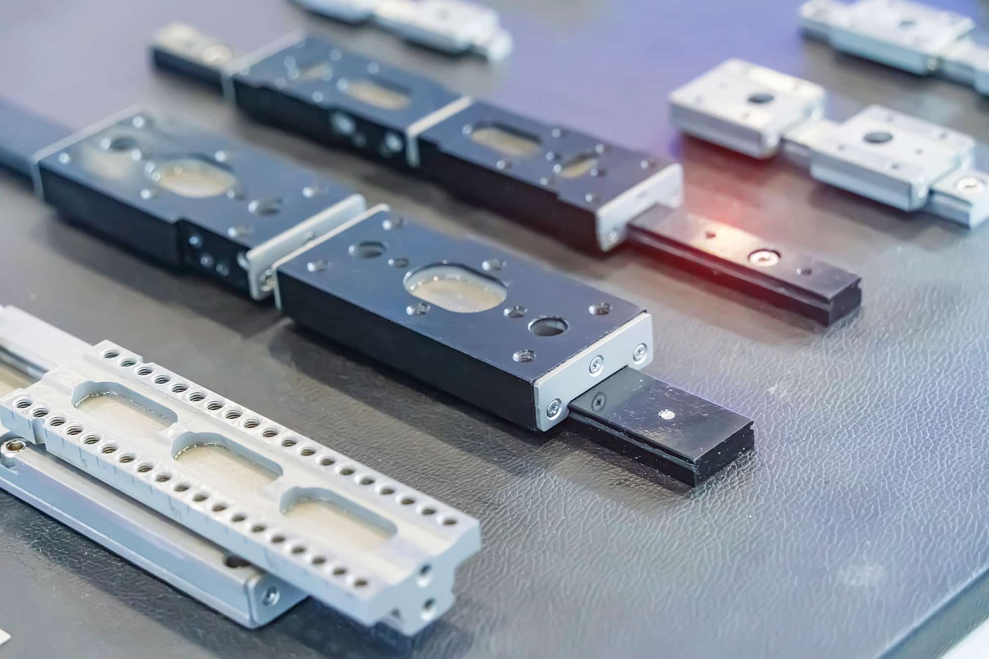 Close-up of gray and black modular metal blocks with circular holes on a textured table surface on a workstation.